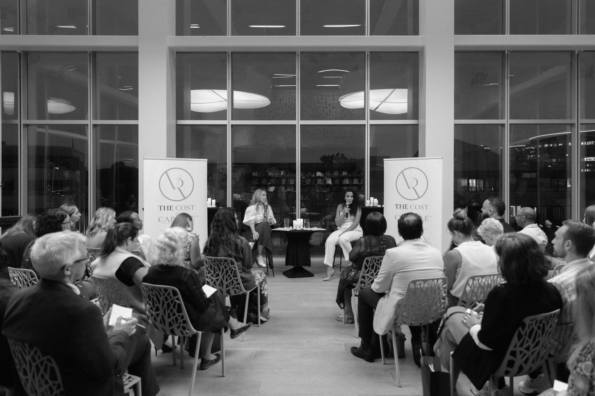 Verena Rizg on stage at the Halifax launch of The Cost of Capable, August 2026, a full house at blue hour.